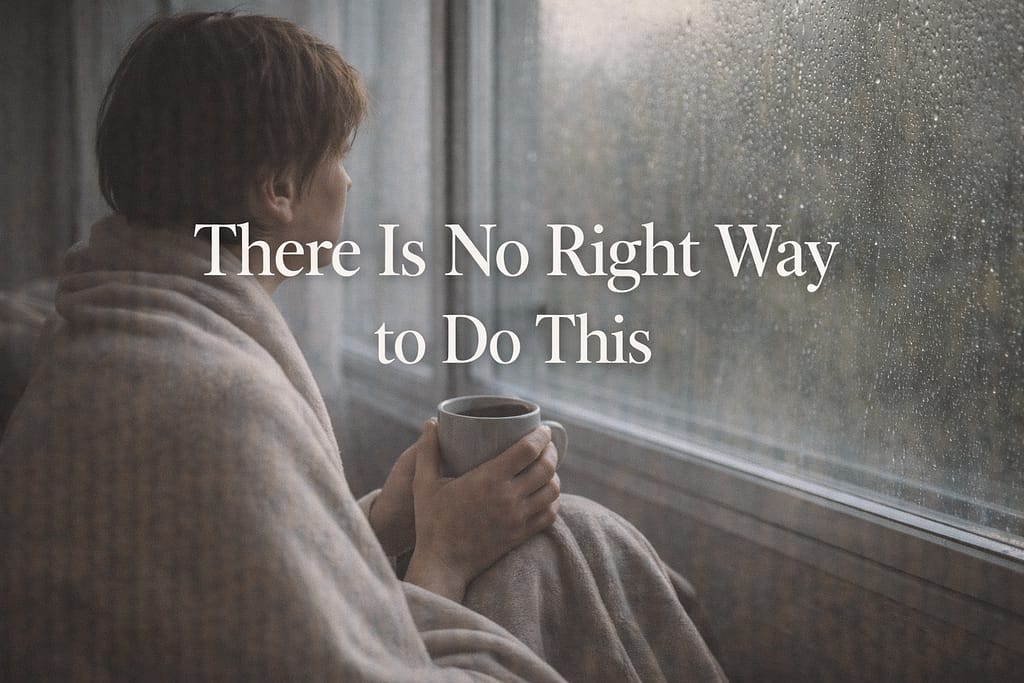 Person wrapped in a blanket by a rainy window holding a mug, representing the permission to sit with grief without trying to fix it